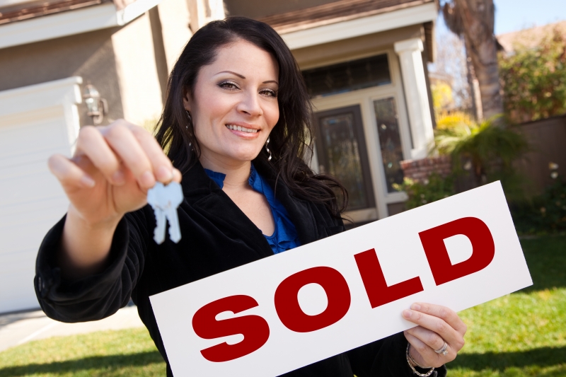 932935-hispanic-woman-holding-keys-and-sold-sign-in-front-of-house